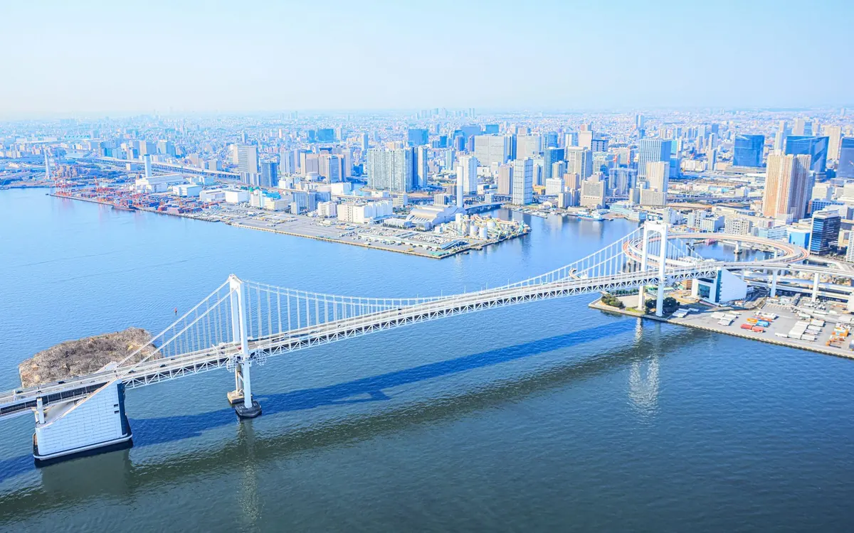 Eine weiße Hängebrücke über die Tokyo Bay mit Türmen am Ufer dahinter