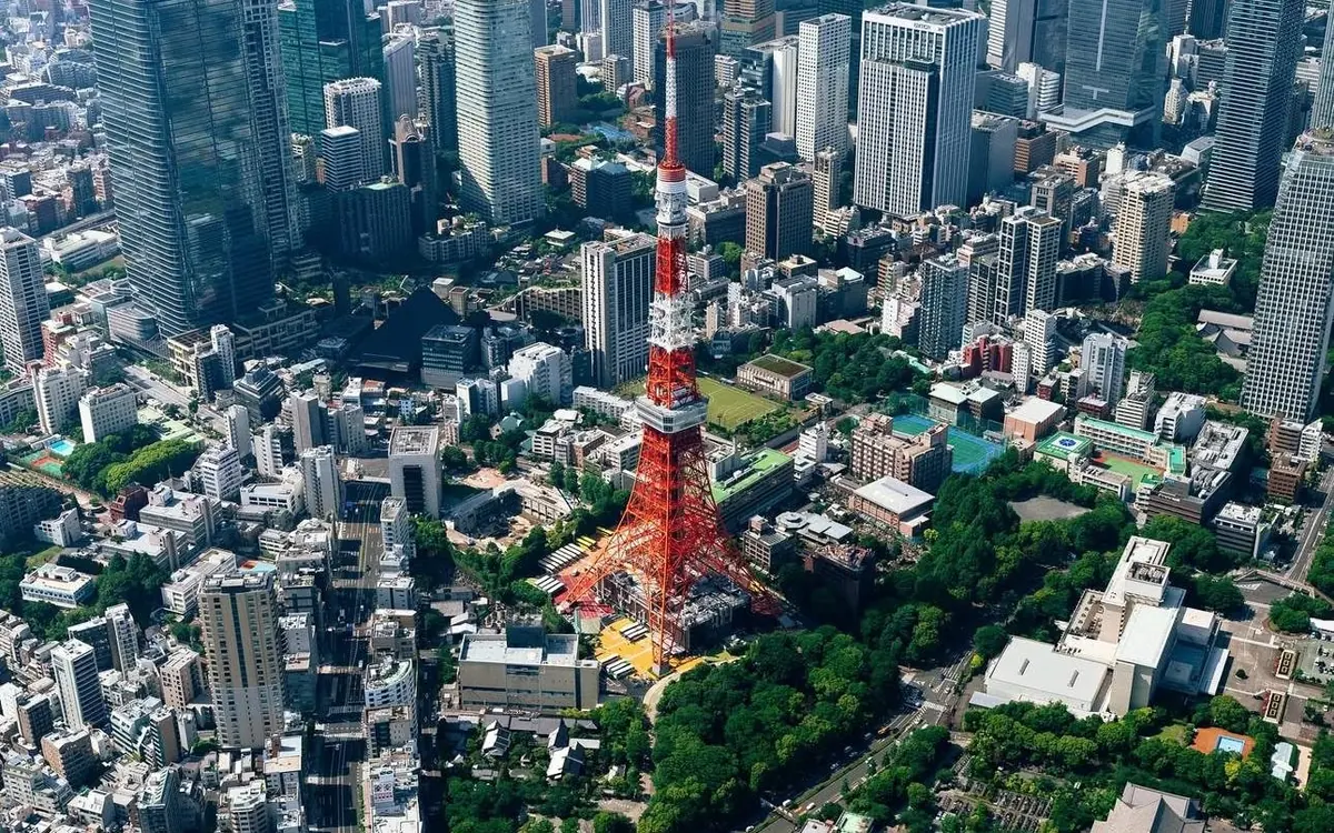 The red and white lattice tower seen from the air in daylight, surrounded by dense blocks and green parkland